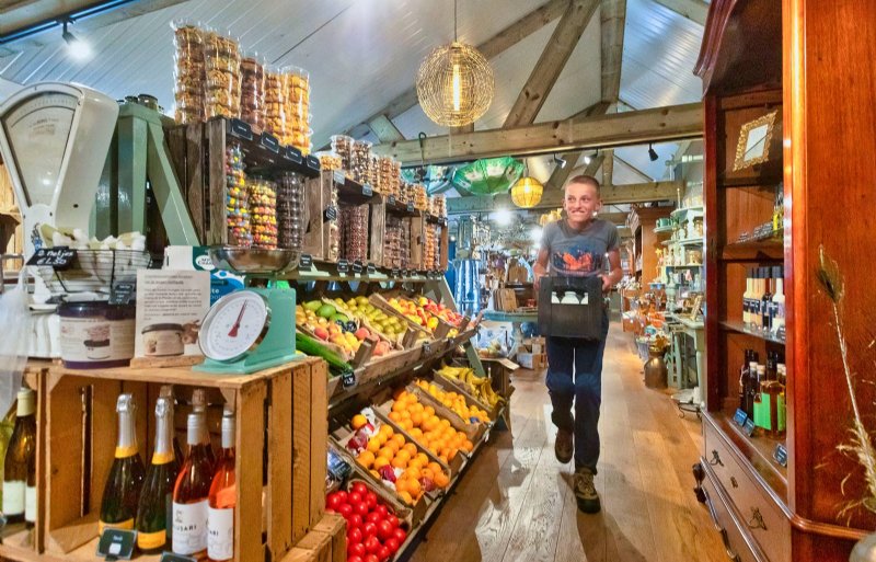 Zorgdeelnemer Milan snelt door het gangpad in een kruising van boerderijwinkel, delicatessenzaak en cadeauwinkel.